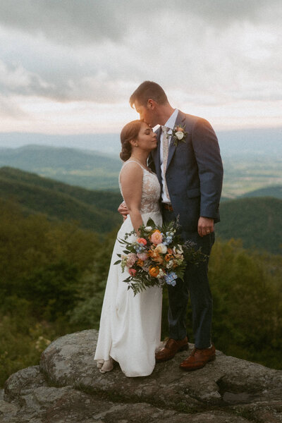 Groom in a blue suit kissing the bride on the forehead during their elopement in Shenandoah National Park.