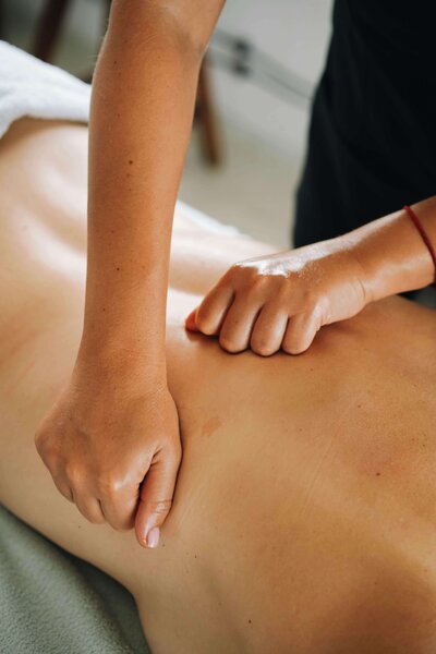 A person receives a deep tissue massage; a massage therapist in Tolleson, Arizona uses their fists and knuckles to apply pressure along the person's bare back during message therapy.
