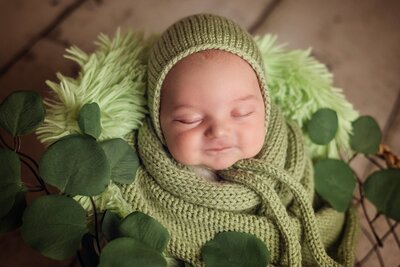 An adorable baby in a green knitted hat, comfortably nestled in a matching green blanket, showcasing pure sweetness.