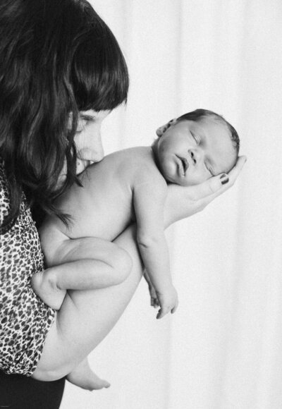 mom kissing back of newborn baby while she sleeps in her arms