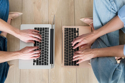 overview of two women typing on laptop sitting on floor