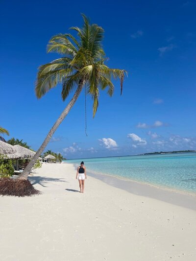 junge Frau spaziert an Strand entlang mit türkisblauem Wasser und wunderschöner Palme