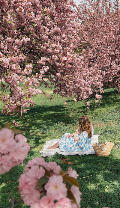 Anna Page sitting on a picnic blanket in a park full of cherry blossons