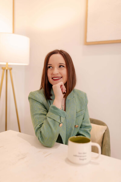 Woman wearing green blazer and smiling looking away from camera