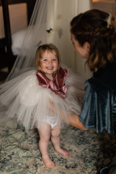 bridesmaid putting dress on a smiling little girl