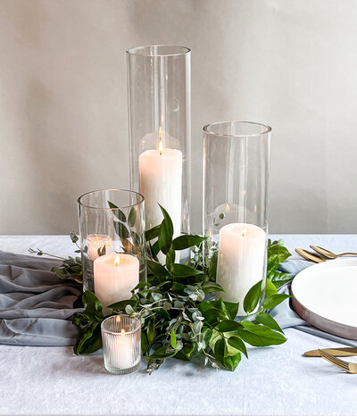 Candles in clear vases decorated with greenery on a table