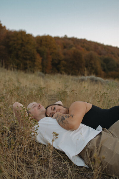 A couple lying in a field outside during the Fall season. A woman is laying on her man's chest.
