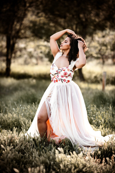 Gorgeous mother wearing a flowy white dress in a lush field at sunset. 
