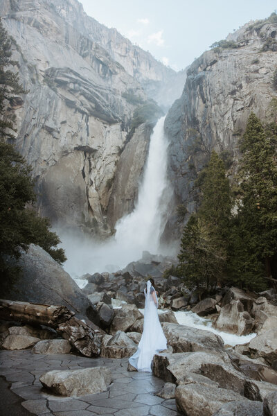 Bride’s veil blowing in waterfall mist during Yosemite elopement
