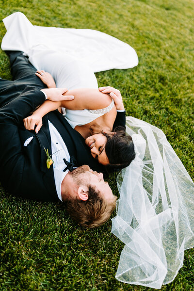 A photo of a bride and groom laying in the grass hugging one another laughing in Connecticut