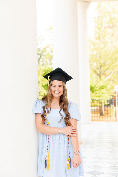 Graduate in cap and gown smiling beside white columns on a Birmingham campus — Madison Abernathy Photo
