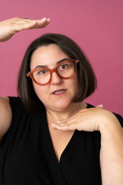Headshot of Founder Sydney in black shirt with pink background
