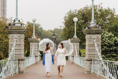 two brides walk hand in hand under umbrellas in boston public garden