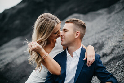 Bride & groom kissing while seated on rock