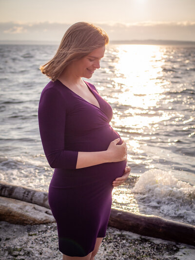 A pregnant woman holds her belly at Carkeek Park, WA.