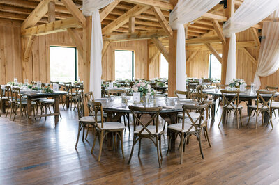 Rustic-chic wedding reception setup with round tables, cross-back chairs, floral centerpieces, and exposed wooden beams at Bear Ridge Destination.

