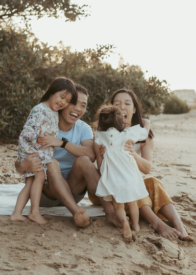 Sydney family of four hugging and laughing at the beach.