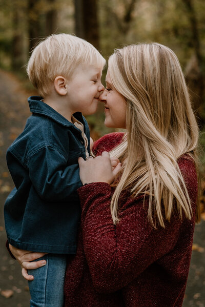 Mom wearing red shirt holding her toddler son while his kissing her on the nose at Patapsco State Park in Maryland