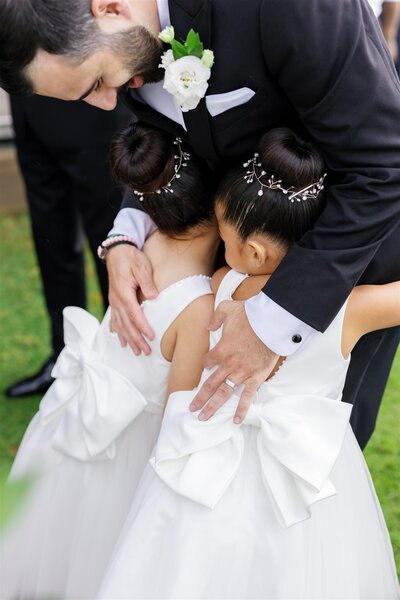 A newlywed leaning down and hugging two small kids in dresses 