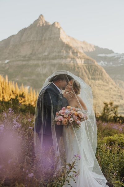 Montana bride and groom kissing under her veil with mountain views in Glacier National Park.