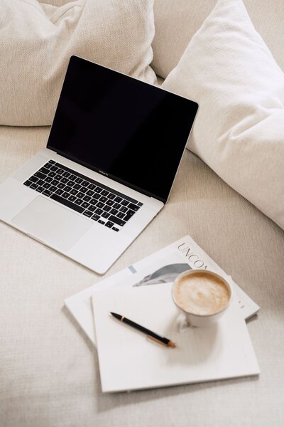 Laptop  on a beige sofa with cream books and a coffee