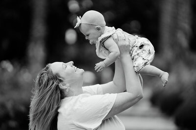 Black and white portrait of a mother in Geelong joyfully lifting her baby girl into the air during an outdoor family session.







