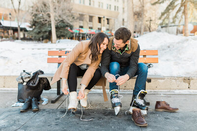 Couple sitting on a bench and tying their skates while laughing in Calgary, Ab.