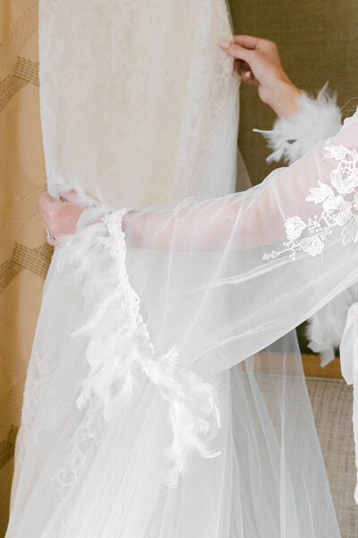 A delicate close-up of a bride holding her wedding dress at The Westin Hotel in Savannah. The intricate lace, feathered sleeves, and sheer fabric add an ethereal touch, capturing the elegance and romance of a luxury wedding.