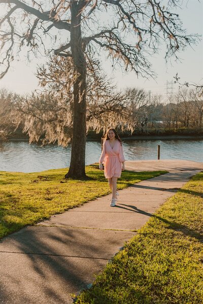 Teen girl celebrating her 16th birthday by walking along a lakeside path at Walter Hall Park. Surrounded by trees and natural scenery, she enjoys a peaceful moment in the golden light. 