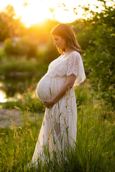 Pregnant women wearing a white dress, looking at her belly in a field in Ottawa
