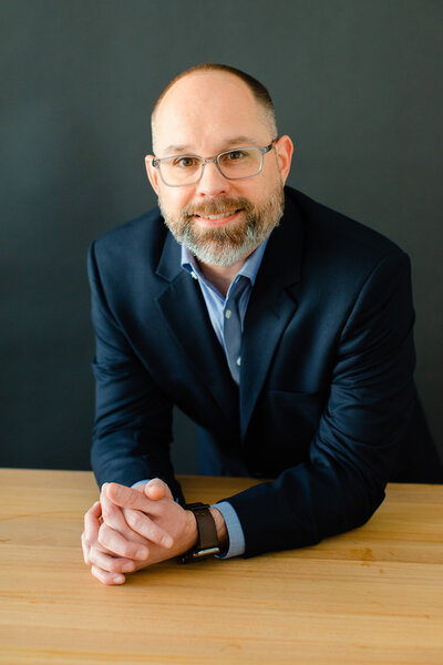 a professional studio headshot of founder josh hester in a navy  shirt and jacket