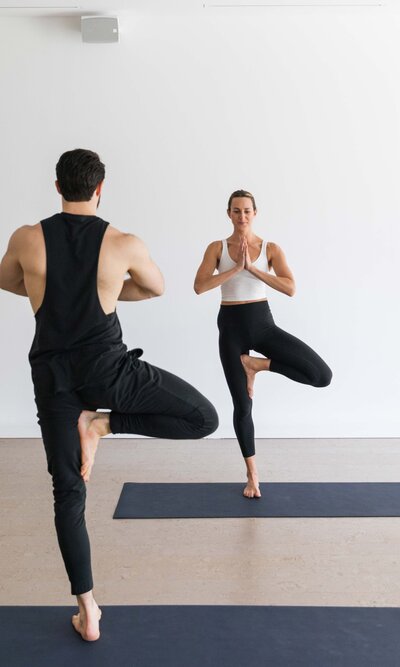 Yoga instructor guiding a male client in tree pose, both practicing balance and mindfulness together.