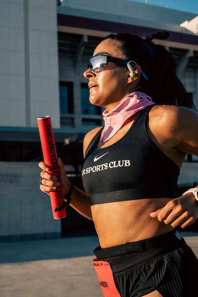 Close-up of a HER Sports Club runner holding a relay baton during training.