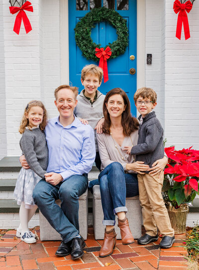 Family of five sitting in front of a blue door and white wall