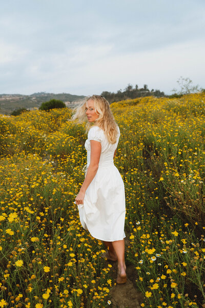 a girl walking through a field of flowers looking over her shoulder