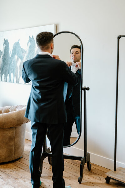 Groom straightening his bowtie in mirror