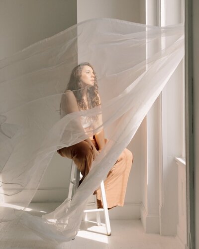 Photo of a business owner in a sunlit window behind a gauzy curtain | Branding Photography | Woman Owned Business |