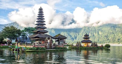 A serene waterside view of a traditional Balinese temple, surrounded by lush greenery and reflected in a calm lake under a clear blue sky. This tranquil and culturally rich destination highlights the unforgettable experiences offered through vacation fundraising for charities.