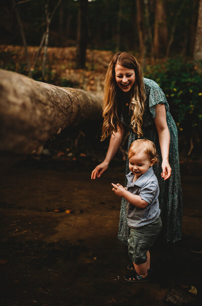 Family photographers Maryland captures mommy and me session with mother in a green dress walking with her toddler son in the woods