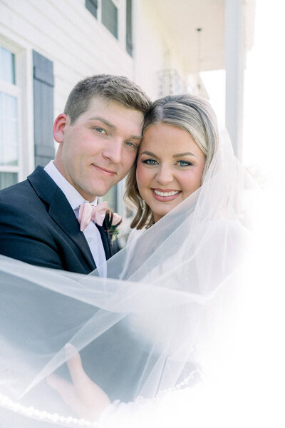 Bride and groom pose under a flowing veil in soft natural light. A classic love story by Jackson Ms Wedding Photographer.