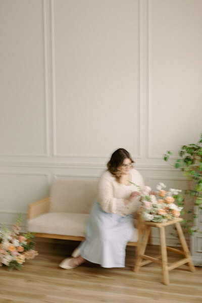 A blurry photo of wedding planner, Zelie & Co., fixing a floral arrangement on a stool