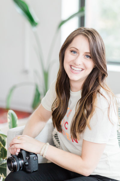 photo of the brand photographer, Laurelyn of My Brand Photographer, sitting on a vintage rug next to a stack of books, wearing a yellow long-sleeved tee and jeans