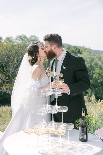 a newlywed couple kissing by a champagne tower