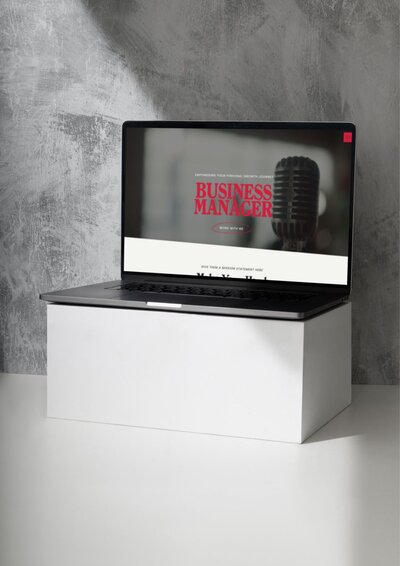  Laptop mockup showing the Long Beach Showit website template homepage. The design features bold red typography reading “Business Manager” next to a vintage-style microphone photo on a muted gray background, blending modern structure with retro flair. The laptop rests on a white block against a textured concrete wall backdrop.