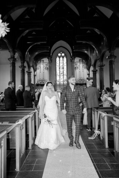 black and white shot of bride and groom walking out of church