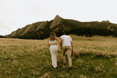 Couple holding hands and walking towards the mountains at Chautauqua Park in Colorado
