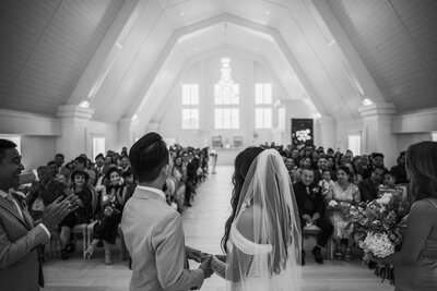 Black and white image of bride and groom holding hands while looking at their wedding guests