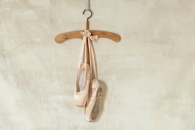 Pair of ballet slippers hanging on a wooden hanger against a soft wall, symbolizing grace, resilience, and the hopeful journey of adoption.