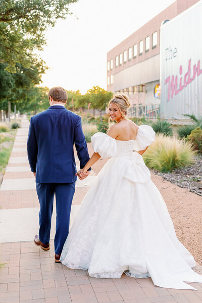 Bride and groom walk together into the glow of a sunset 