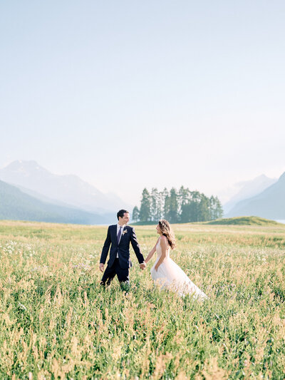 Bride and groom walking in field between mountains